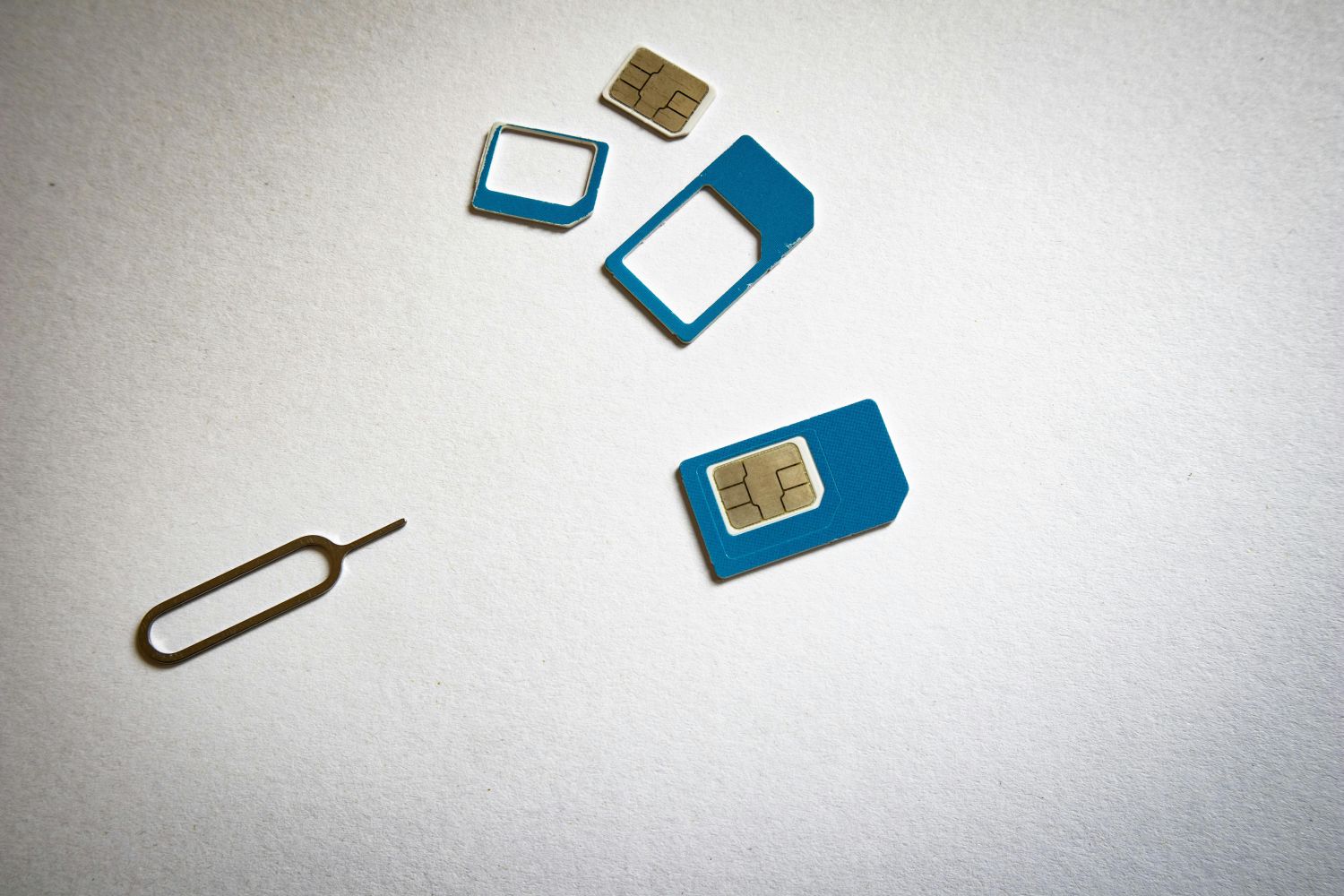 visualys- Eine SIM-Karte mit blauen Adaptern, eine Micro- und Nano-SIM-Karte und ein SIM-Karten-Auswurfwerkzeug sind auf einer weißen Fläche angeordnet.