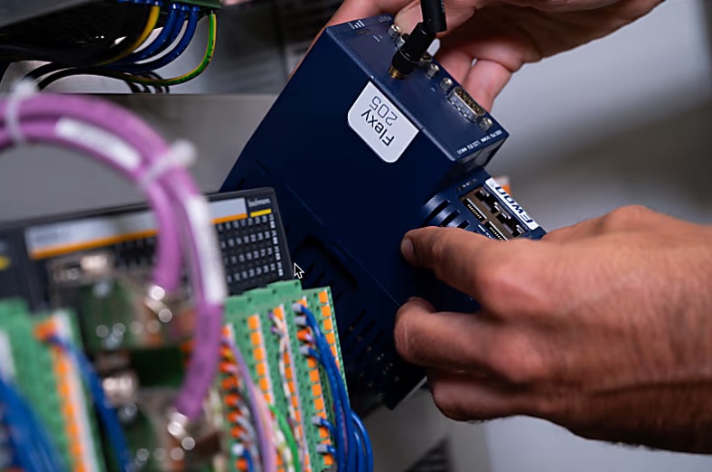 Hands connecting a blue FELXY 205 device to a control panel with colored wires and electronic components—an easy start in IIoT, powered by InHand Networks’ advanced technology.