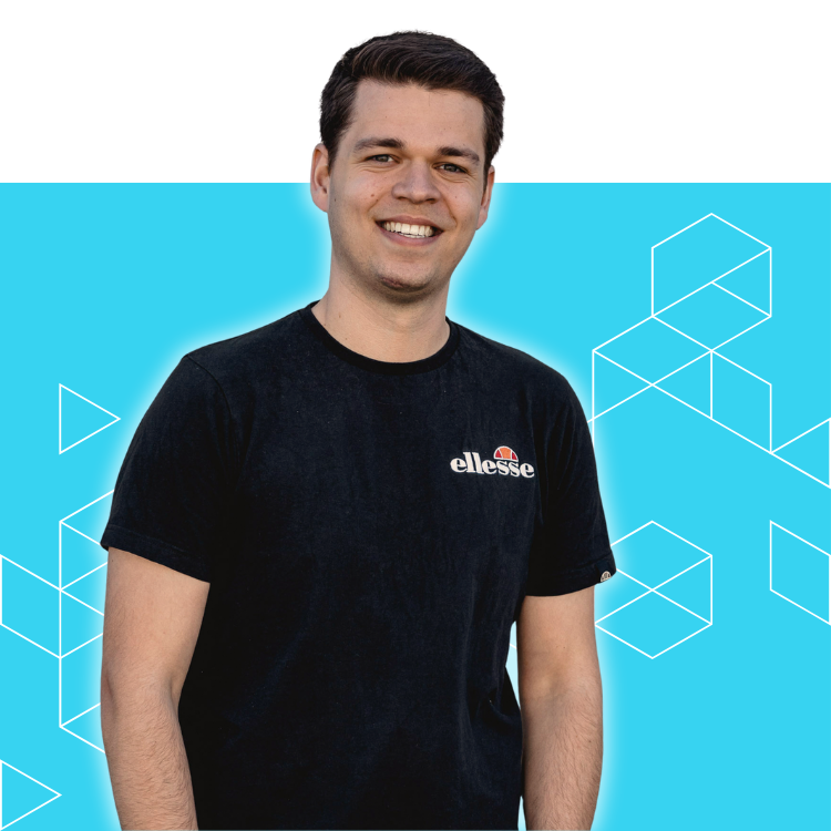 A young man in a black ellesse t-shirt stands smiling in front of a bright blue background with white geometric shapes.