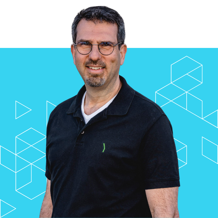 A man with short dark hair, glasses, and a goatee is smiling. He wears a black polo shirt over a white t-shirt. The background is bright blue with geometric white line patterns.